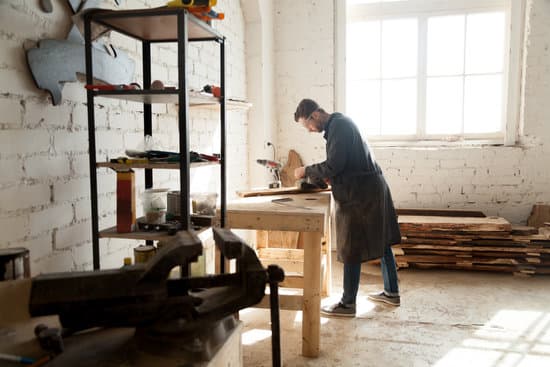 Side view of professional young joiner woodworking in planing shop garage. Skilled craftsman working on customized furniture, using sander. Carpentry services for construction, renovation and repair