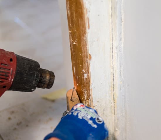 Detail of removing old white paint from door frame with heat gun and scraper