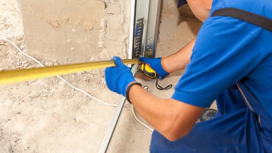 Building improvement concept. Panoramic and cropped view of professional worker using measure tape and install metal rail on garage door system in new house under construction