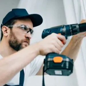 adult-repairman-in-goggles-fixing-window-handle-by-electric-drill